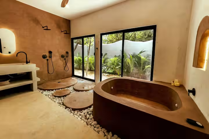 Tinez Suite — wooden soaking tub beside dual showers with jungle views
