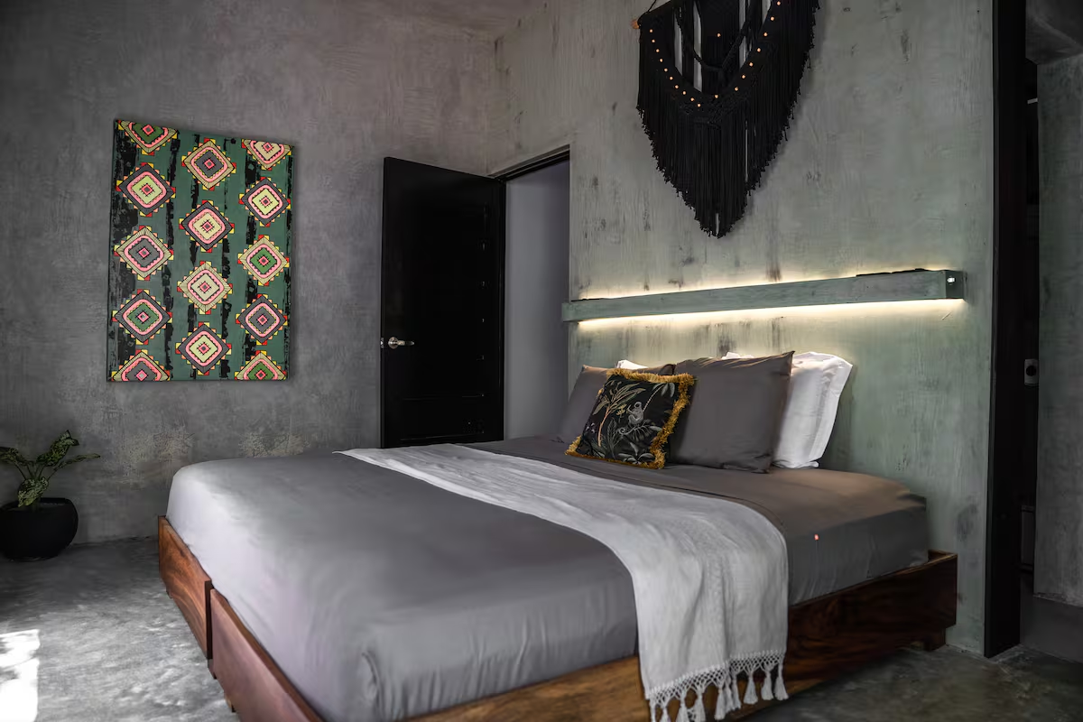 Ferro Suite — moody concrete bedroom with king bed, backlit headboard, and geometric artwork